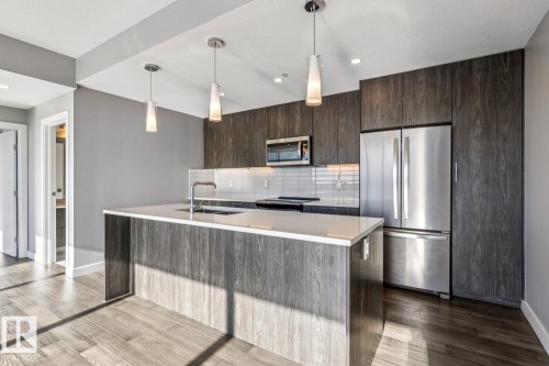Kitchen with stainless steel appliances, dark wood finish cabinetry, decorative light fixtures, a kitchen island with sink, and light stone countertops - 3300 10180 103 Street, Edmonton, AB - Indoor Photo Showing Kitchen With Stainless Steel Kitchen With Upgraded Kitchen