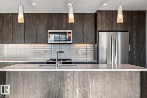 Kitchen featuring modern cabinets, stainless steel appliances, a center island with sink, pendant lighting, and light stone counters - 3300 10180 103 Street, Edmonton, AB - Indoor Photo Showing Kitchen With Stainless Steel Kitchen With Upgraded Kitchen