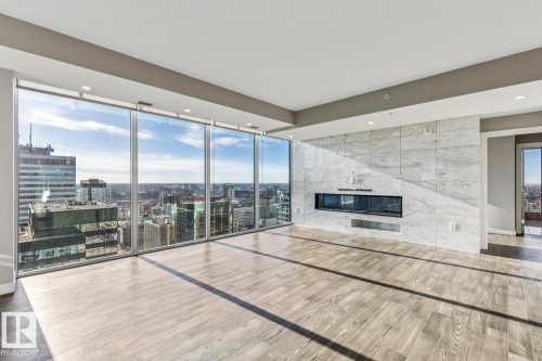 Unfurnished living room featuring floor to ceiling windows, wood finished floors, a tiled fireplace, recessed lighting, and a city view - 3300 10180 103 Street, Edmonton, AB - Indoor With Fireplace