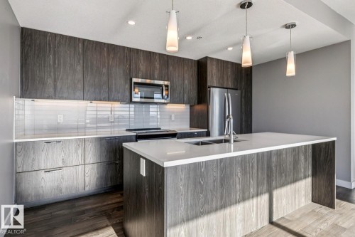 Kitchen featuring modern cabinets, backsplash, decorative light fixtures, dark wood finish cabinets, and stainless steel appliances - 3300 10180 103 Street, Edmonton, AB - Indoor Photo Showing Kitchen With Stainless Steel Kitchen With Upgraded Kitchen