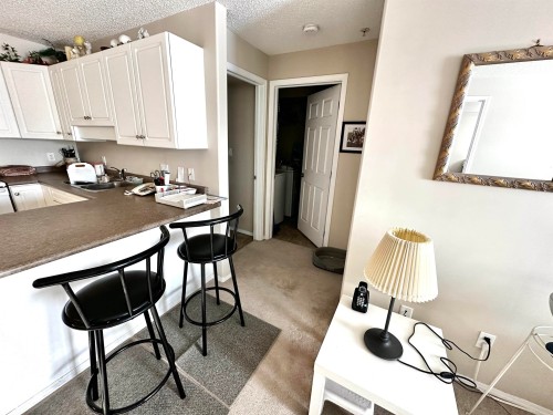 Kitchen featuring a breakfast bar area, dark countertops, a textured ceiling, white cabinetry, and light colored carpet - 215 13625 34 Street, Edmonton, AB - Indoor Photo Showing Kitchen
