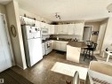 Kitchen featuring dark countertops, white appliances, a peninsula, a breakfast bar area, and a textured ceiling - 215 13625 34 Street, Edmonton, AB  - Indoor Photo Showing Kitchen With Double Sink 