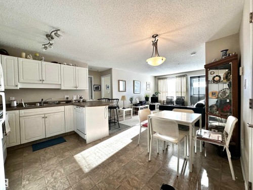 Kitchen featuring dark countertops, a peninsula, decorative light fixtures, white cabinets, and a textured ceiling - 215 13625 34 Street, Edmonton, AB - Indoor