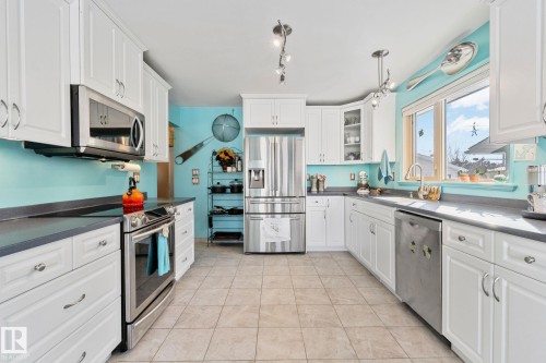 Kitchen featuring stainless steel appliances, white cabinets, dark countertops, glass insert cabinets, and rail lighting - 4231 39 Avenue, Leduc, AB - Indoor Photo Showing Kitchen With Stainless Steel Kitchen With Upgraded Kitchen