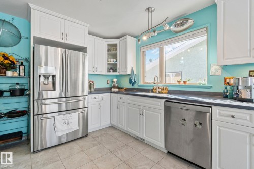 Kitchen with stainless steel appliances, dark countertops, white cabinetry, glass insert cabinets, and decorative light fixtures - 4231 39 Avenue, Leduc, AB - Indoor Photo Showing Kitchen