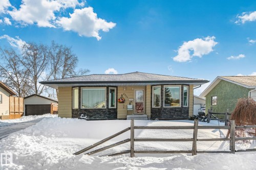 Snow covered property with covered porch, stone siding, an outbuilding, a garage, and roof with shingles - 4231 39 Avenue, Leduc, AB - Outdoor