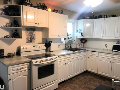 Kitchen with electric stove, white cabinetry, open shelves, and light countertops - 4735 48 Ave, Evansburg, AB - Indoor Photo Showing Kitchen With Double Sink