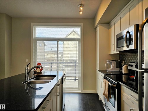 Kitchen with stainless steel appliances, dark stone countertops, dark wood-style flooring, an island with sink, and a textured ceiling - 129 2560 Pegasus Boulevard, Edmonton, AB - Indoor Photo Showing Kitchen With Double Sink