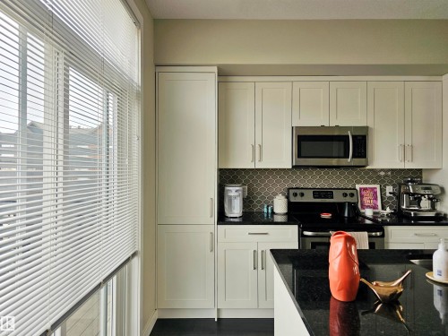 Kitchen with white cabinets, stainless steel appliances, dark stone countertops, and decorative backsplash - 129 2560 Pegasus Boulevard, Edmonton, AB - Indoor Photo Showing Kitchen