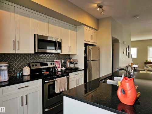 Kitchen featuring stainless steel appliances, white cabinetry, and dark stone counters - 129 2560 Pegasus Boulevard, Edmonton, AB - Indoor Photo Showing Kitchen With Double Sink With Upgraded Kitchen