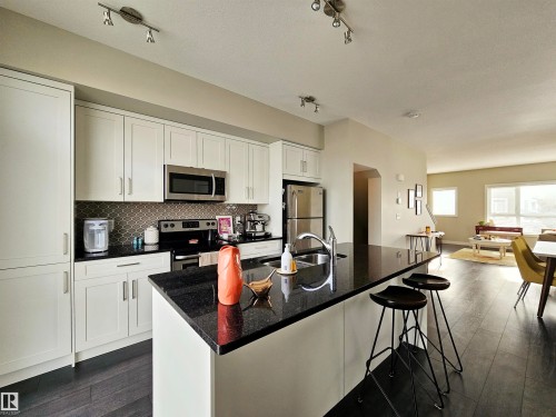 Kitchen featuring white cabinetry, dark wood finished floors, a breakfast bar, stainless steel appliances, and rail lighting - 129 2560 Pegasus Boulevard, Edmonton, AB - Indoor Photo Showing Kitchen With Upgraded Kitchen