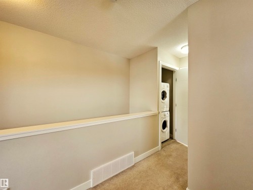 Corridor featuring stacked washer and dryer, carpet flooring, and a textured ceiling - 129 2560 Pegasus Boulevard, Edmonton, AB - Indoor Photo Showing Other Room