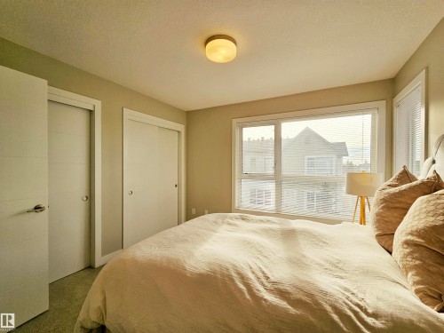 Carpeted bedroom with two closets and a textured ceiling - 129 2560 Pegasus Boulevard, Edmonton, AB - Indoor Photo Showing Bedroom
