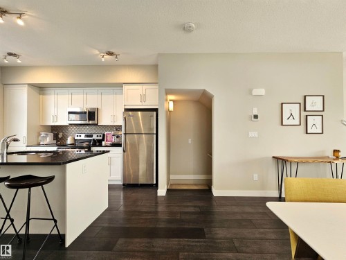 Kitchen with stainless steel appliances, dark wood-type flooring, white cabinetry, backsplash, and arched walkways - 129 2560 Pegasus Boulevard, Edmonton, AB - Indoor Photo Showing Kitchen
