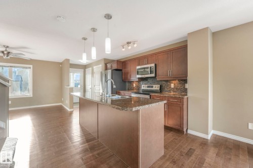 Kitchen with stainless steel appliances, dark stone countertops, a ceiling fan, a center island with sink, and decorative backsplash - 385 Secord Boulevard, Edmonton, AB - Indoor Photo Showing Kitchen With Double Sink With Upgraded Kitchen
