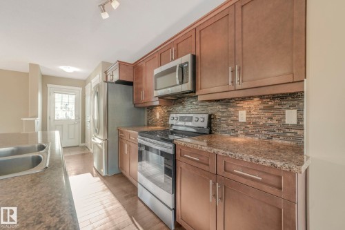 Kitchen featuring stainless steel appliances, wood finish cabinets, light wood-type flooring, backsplash, and dark stone counters - 385 Secord Boulevard, Edmonton, AB - Indoor Photo Showing Kitchen With Double Sink