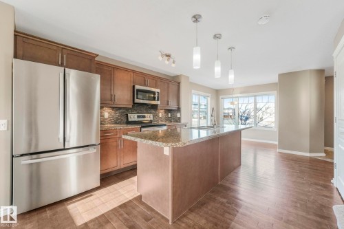 Kitchen with stainless steel appliances, hanging light fixtures, decorative backsplash, an island with sink, and dark stone counters - 385 Secord Boulevard, Edmonton, AB - Indoor Photo Showing Kitchen With Upgraded Kitchen
