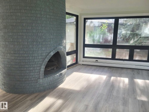 Unfurnished living room featuring a brick fireplace, baseboard heating, and wood finished floors - 9535 147 Avenue, Edmonton, AB - Indoor With Fireplace