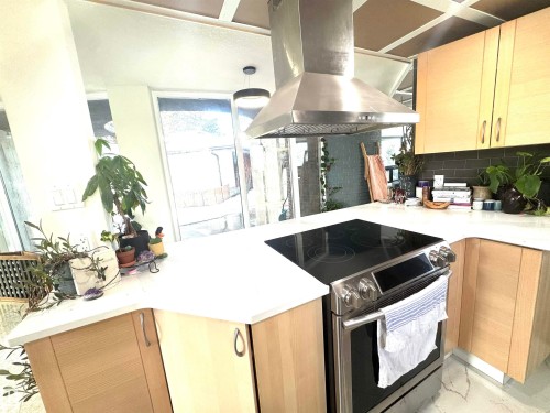 Kitchen featuring stainless steel electric stove, a peninsula, island exhaust hood, light brown cabinetry, and tasteful backsplash - 9535 147 Avenue, Edmonton, AB - Indoor Photo Showing Kitchen