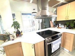 Kitchen featuring stainless steel electric stove, a peninsula, island exhaust hood, light brown cabinetry, and tasteful backsplash - 