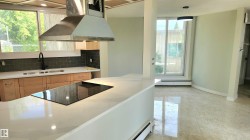 Kitchen with ventilation hood, light stone counters, a baseboard heating unit, decorative backsplash, and black electric stovetop - 