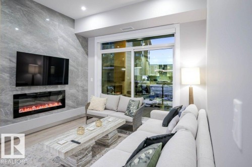 Living area featuring a large fireplace, wood finished floors, and tile walls - 101 7471 May Common, Edmonton, AB - Indoor Photo Showing Living Room With Fireplace
