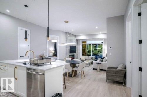 Kitchen with hanging light fixtures, white cabinets, light stone counters, open floor plan, and a breakfast bar area - 101 7471 May Common, Edmonton, AB - Indoor Photo Showing Kitchen With Upgraded Kitchen