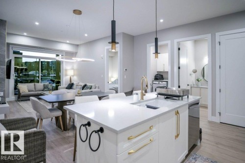 Kitchen featuring white cabinets, decorative light fixtures, light wood-type flooring, an island with sink, and recessed lighting - 101 7471 May Common, Edmonton, AB - Indoor Photo Showing Kitchen