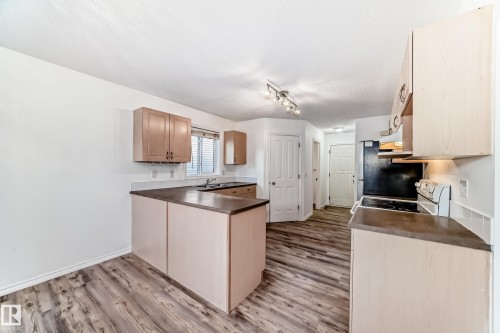 Kitchen featuring light wood finish cabinets, dark countertops, light wood-type flooring, electric stove, and a peninsula - 4604 202 Street, Edmonton, AB - Indoor Photo Showing Kitchen
