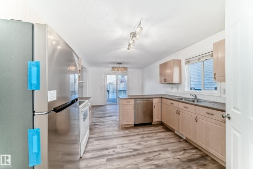 Kitchen featuring stainless steel appliances, a peninsula, light wood finish cabinets, a textured ceiling, and light wood-style flooring - 4604 202 Street, Edmonton, AB - Indoor Photo Showing Kitchen With Double Sink