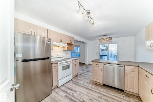 Kitchen featuring stainless steel appliances, light wood finish cabinets, a textured ceiling, light wood finished floors, and a peninsula - 4604 202 Street, Edmonton, AB - Indoor Photo Showing Kitchen