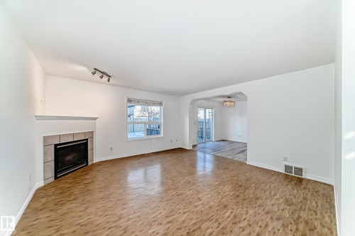 Unfurnished living room featuring light wood-type flooring, arched walkways, a tiled fireplace, and track lighting - 4604 202 Street, Edmonton, AB - Indoor With Fireplace
