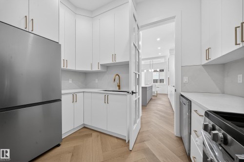 Kitchen featuring white cabinets, appliances with stainless steel finishes, parquet flooring, recessed lighting, and light stone counters - 132 29 Street, Edmonton, AB - Indoor Photo Showing Kitchen