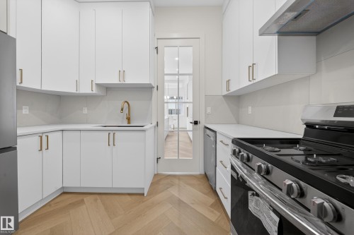 Kitchen featuring appliances with stainless steel finishes, white cabinets, exhaust hood, parquet flooring, and light stone countertops - 132 29 Street, Edmonton, AB - Indoor Photo Showing Kitchen
