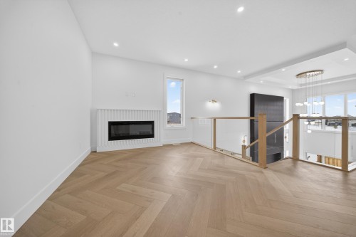 Unfurnished living room featuring a chandelier, a glass covered fireplace, parquet flooring, and recessed lighting - 132 29 Street, Edmonton, AB - Indoor Photo Showing Living Room With Fireplace