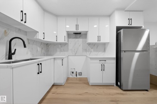Kitchen featuring white cabinetry, freestanding refrigerator, light wood finished floors, tasteful backsplash, and light stone countertops - 132 29 Street, Edmonton, AB - Indoor Photo Showing Kitchen With Double Sink