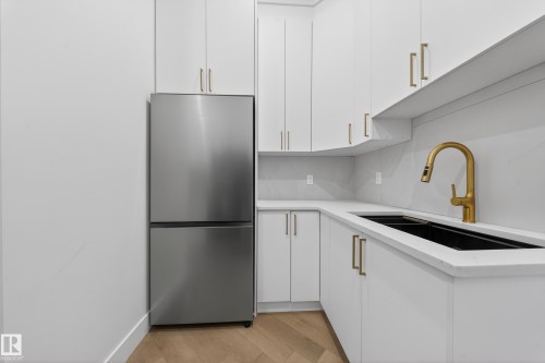 Kitchen featuring stainless steel fridge, white cabinets, light wood finished floors, and light stone countertops - 132 29 Street, Edmonton, AB - Indoor Photo Showing Kitchen