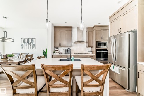 Kitchen featuring decorative light fixtures, stainless steel appliances, a kitchen island with sink, light wood-style flooring, and backsplash - 3569 Erlanger Link, Edmonton, AB - Indoor