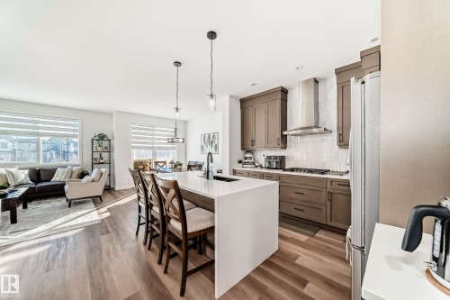 Kitchen featuring decorative light fixtures, decorative backsplash, a breakfast bar, light wood-type flooring, and light stone counters - 3569 Erlanger Link, Edmonton, AB - Indoor