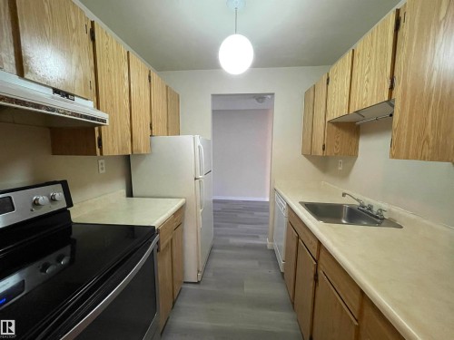 The kitchen features wood cabinetry, a stainless steel sink with a faucet, and a range with an overhead exhaust fan - 311 1624 48 Street, Edmonton, AB - Indoor Photo Showing Kitchen
