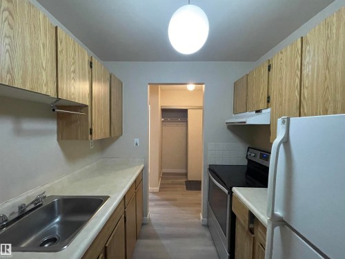 The kitchen features wood cabinetry, a stainless steel sink with a chrome faucet, a white refrigerator, and a stainless steel oven and range - 311 1624 48 Street, Edmonton, AB - Indoor Photo Showing Kitchen