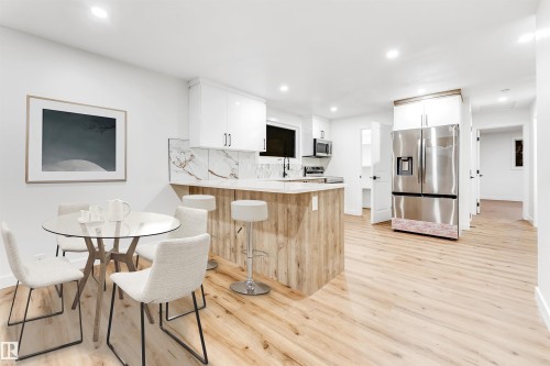 Kitchen featuring stainless steel appliances, a peninsula, white cabinets, backsplash, and light wood finished floors - 4616 32 Avenue, Edmonton, AB - Indoor Photo Showing Dining Room