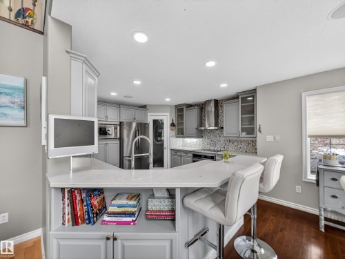 Kitchen with tasteful backsplash, glass fronted cabinets, light stone counters, dark wood finished floors, and stainless steel appliances - 1062 Tory Road, Edmonton, AB - Indoor