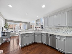 Kitchen featuring gray cabinets, a peninsula, stainless steel dishwasher, dark wood-style flooring, and suspended lighting - 