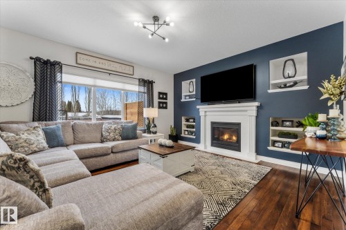 Living area featuring dark wood-type flooring, a glass covered fireplace, and built in features - 13 Heron Link, Spruce Grove, AB - Indoor Photo Showing Living Room With Fireplace
