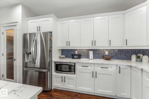 Kitchen featuring stainless steel appliances, light stone countertops, white cabinetry, dark wood finished floors, and tasteful backsplash - 13 Heron Link, Spruce Grove, AB - Indoor Photo Showing Kitchen With Upgraded Kitchen