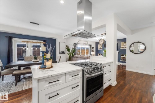 Kitchen featuring stainless steel gas range, white cabinetry, island range hood, and dark wood-style floors - 13 Heron Link, Spruce Grove, AB - Indoor Photo Showing Kitchen With Upgraded Kitchen