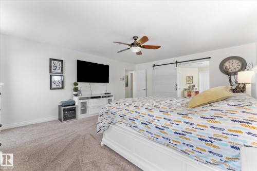 Bedroom featuring a barn door, a ceiling fan, and light carpet - 13 Heron Link, Spruce Grove, AB - Indoor Photo Showing Bedroom