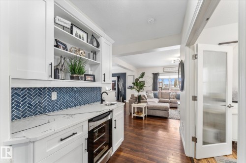 Indoor bar with beverage cooler, white cabinets, light stone counters, dark wood-style floors, and open shelves - 13 Heron Link, Spruce Grove, AB - Indoor