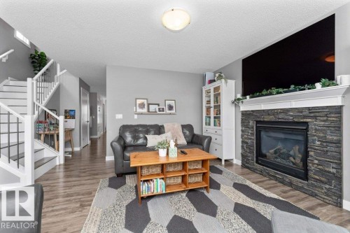 Living room with wood finished floors, a stone fireplace, and a textured ceiling - 2607 20 Avenue, Edmonton, AB - Indoor Photo Showing Living Room With Fireplace